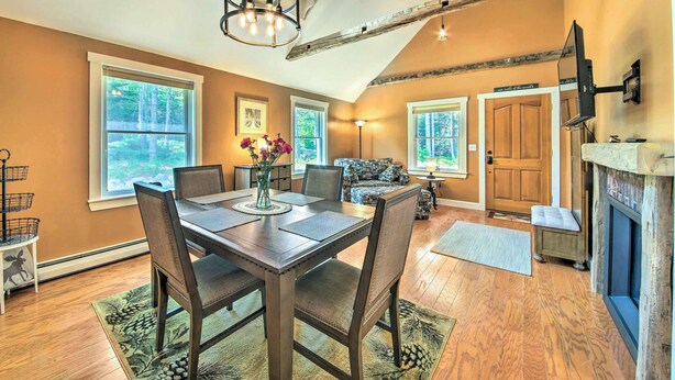 A dining area with a wooden table and chairs, a chandelier, and large windows. - Hidden Gem Cottage' Near Blue Hill Peninsula (Brooklin)