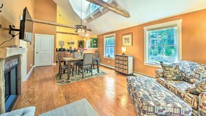 A spacious living area with a fireplace, a dining table with chairs, a sofa, and a large window offering a view of the outdoors. - Hidden Gem Cottage' Near Blue Hill Peninsula (Brooklin)