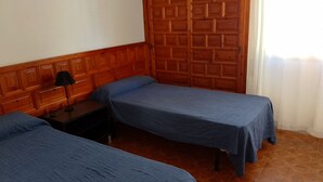 Une chambre avec deux lits simples, une armoire en bois, une table de chevet et une lampe.