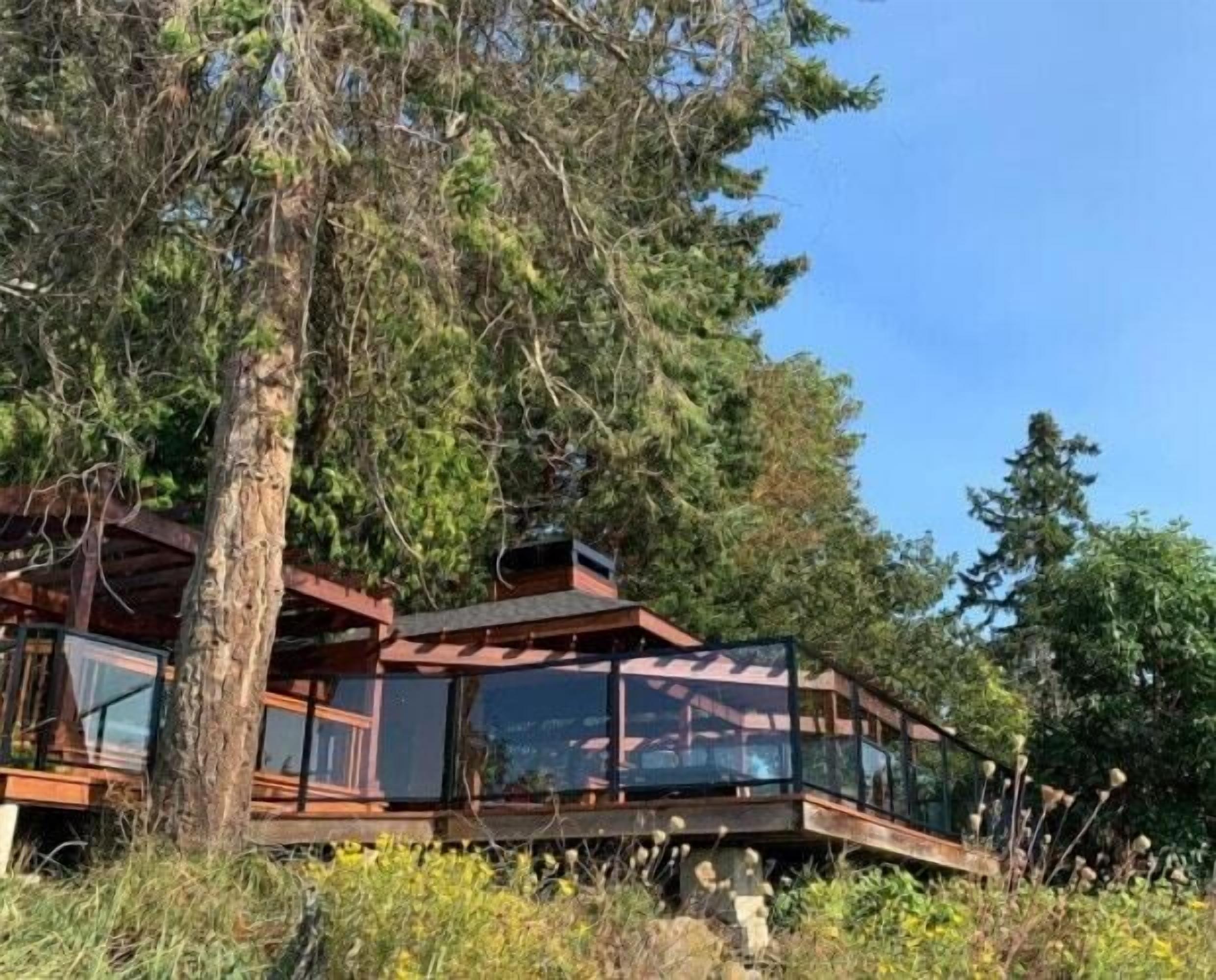 A wooden cabin with a glass balcony, surrounded by trees.