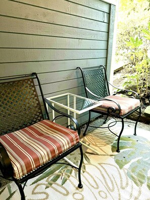 Une terrasse avec deux chaises en métal et une table, une chaise en osier et un tapis à motifs.