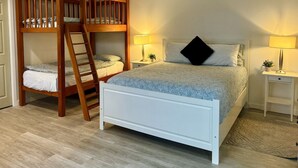 Une chambre avec un lit superposé, un lit simple, deux tables de chevet avec des lampes et une porte.