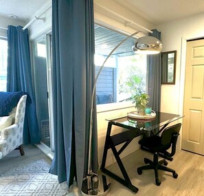 Une pièce comprenant un bureau, une chaise et une grande fenêtre avec des rideaux.