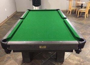 A pool table with a green felt surface and a dark wooden frame.