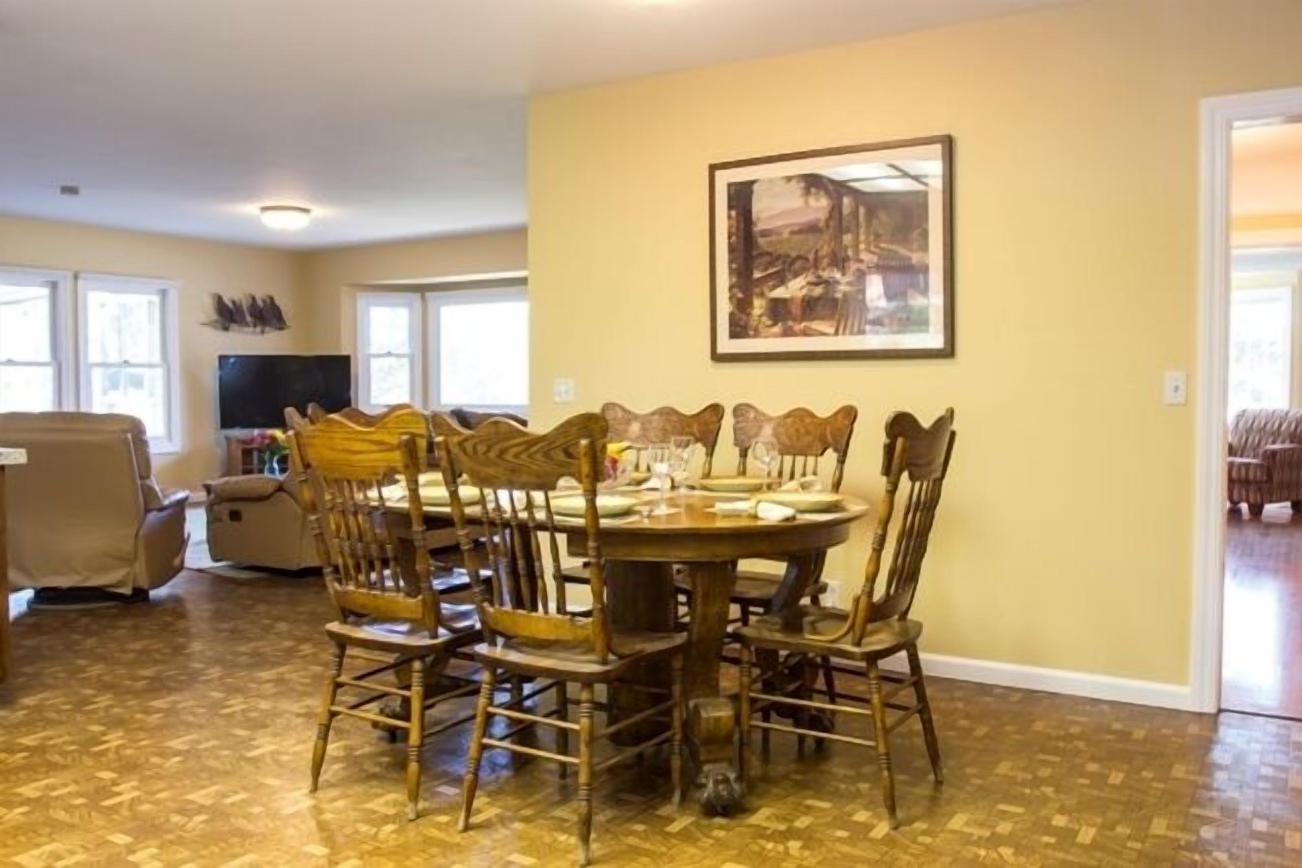 A dining area with a round table and six chairs, a flat-screen TV, and a framed picture on the wall.