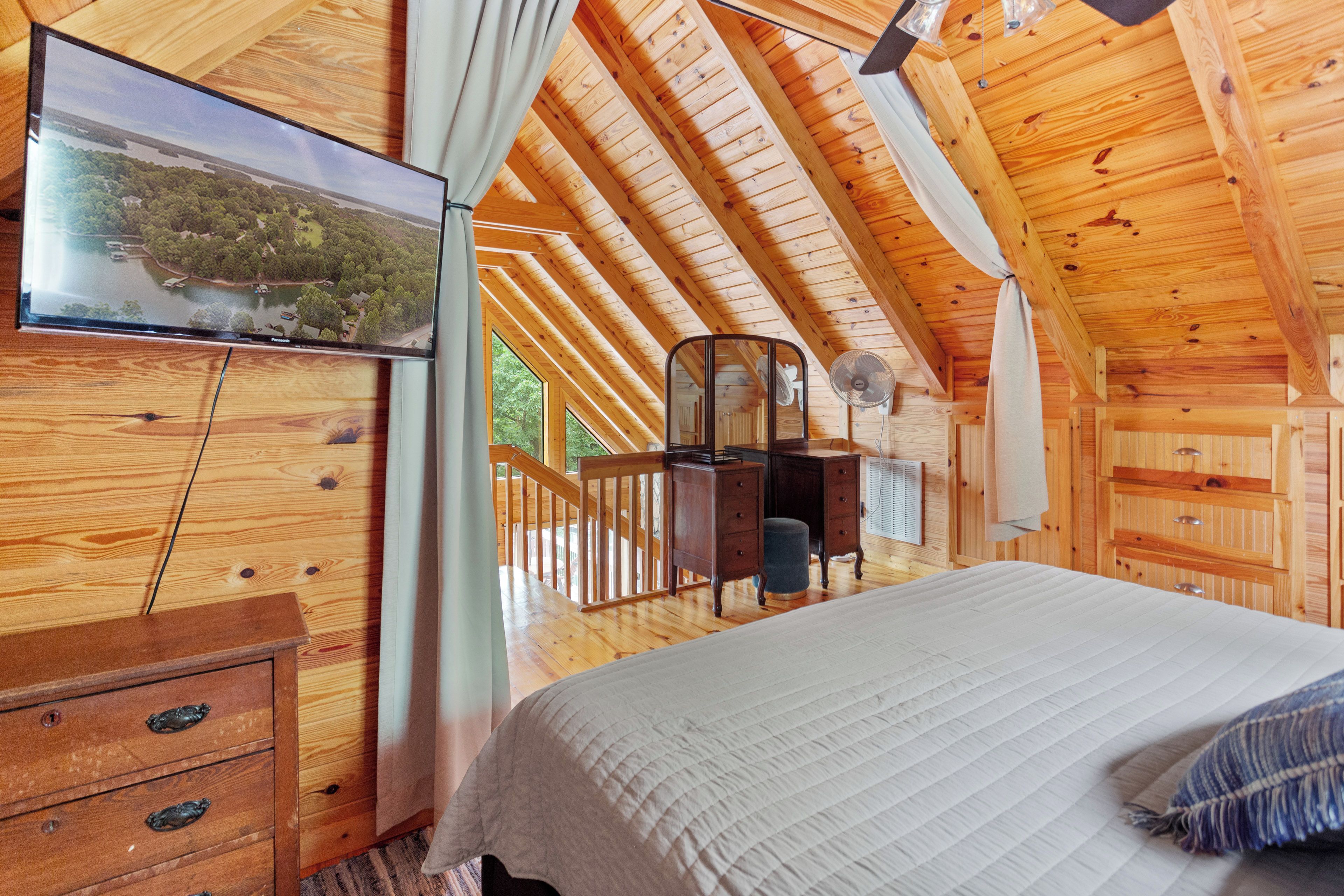 A wooden cabin bedroom with a bed, dresser, and a TV mounted on the wall.