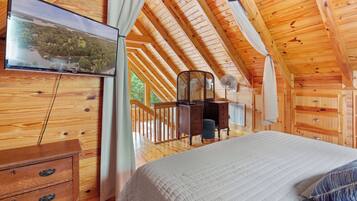 A wooden cabin bedroom with a bed, dresser, and a TV mounted on the wall.