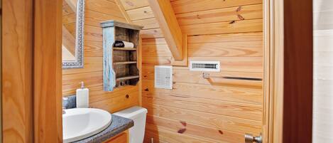 A wooden cabin bathroom with a sink, toilet, and mirror.