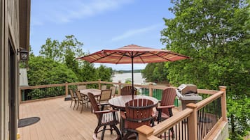 A wooden deck with a table and chairs, a grill, and a view of a lake.