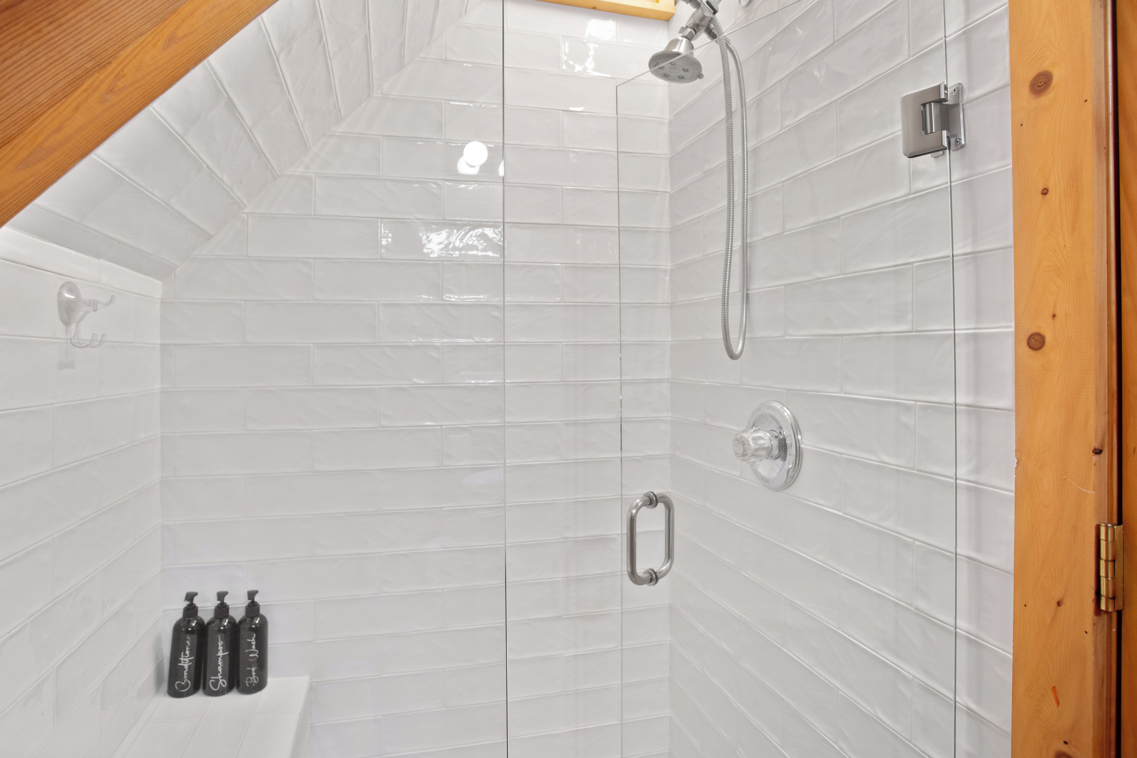 Un área de ducha con paredes de azulejos blancos, techo de madera y ducha de metal.
