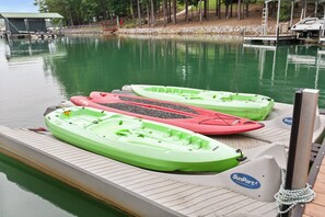 A dock with three kayaks, a covered area, and a boat in the background.