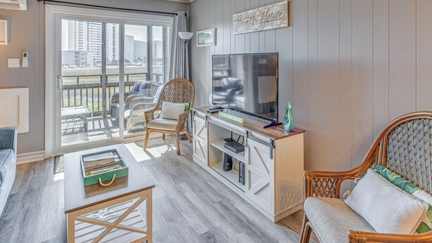 Un salon doté d’un grand téléviseur, de fauteuils en osier, d’un canapé et d’une porte-fenêtre coulissante donnant sur un balcon.