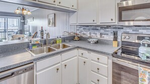 Une cuisine moderne dotée de meubles blancs, de plans de travail en granit, d’appareils électroménagers en acier inoxydable et d’une grande fenêtre donnant sur la ville.