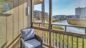 Un balcon avec un fauteuil en osier et une vue sur une rivière et des bâtiments.