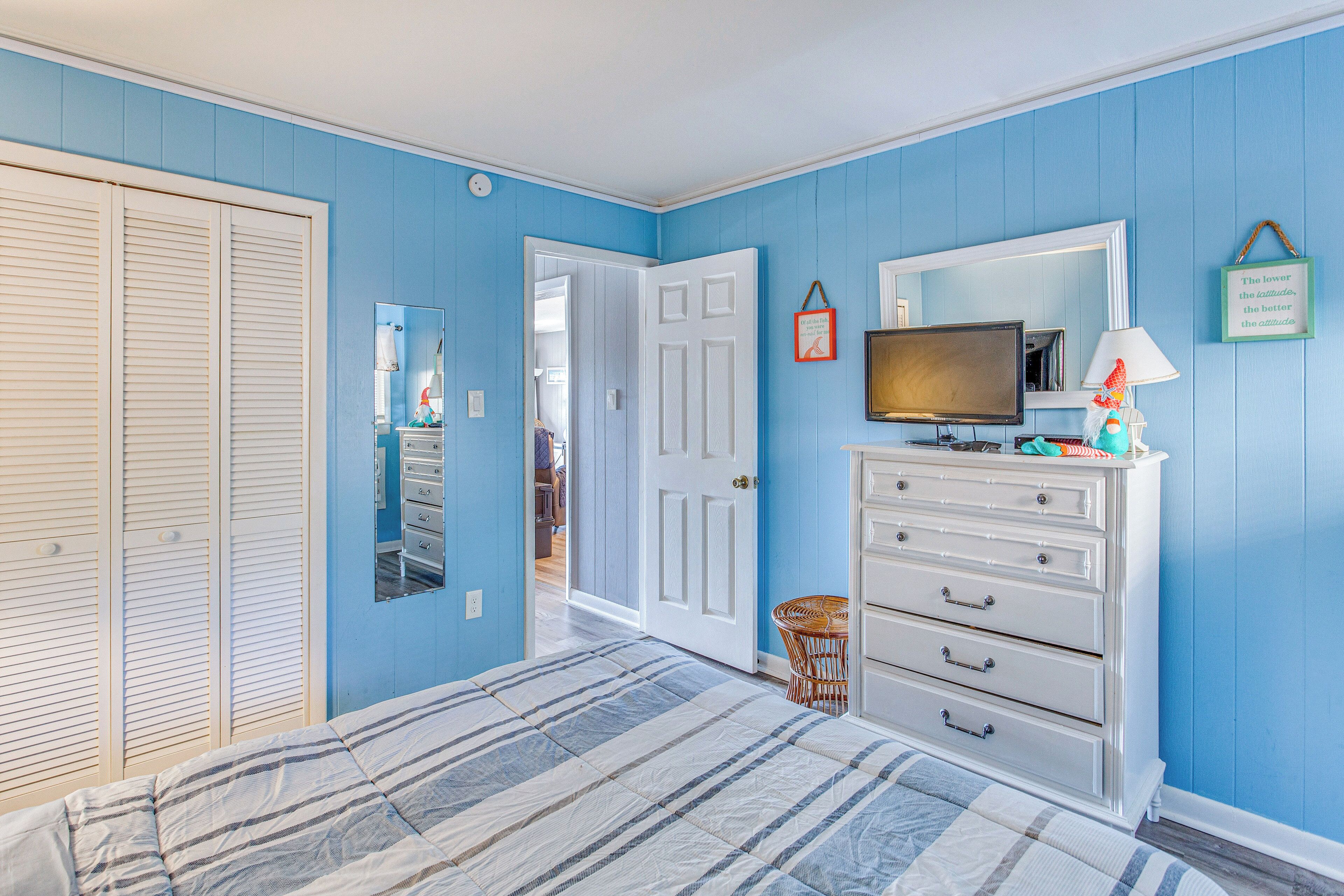 A bedroom with a bed, a dresser, a television, and a door leading to another room.