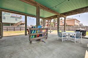 A covered patio area with a wooden table and chairs, a colorful surfboard rack, and a hammock. - 1/2 Mi to Sand: Surfside Beach Retreat! (Freeport)