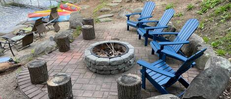 A lakeside patio with Adirondack chairs, a fire pit, and a dock.