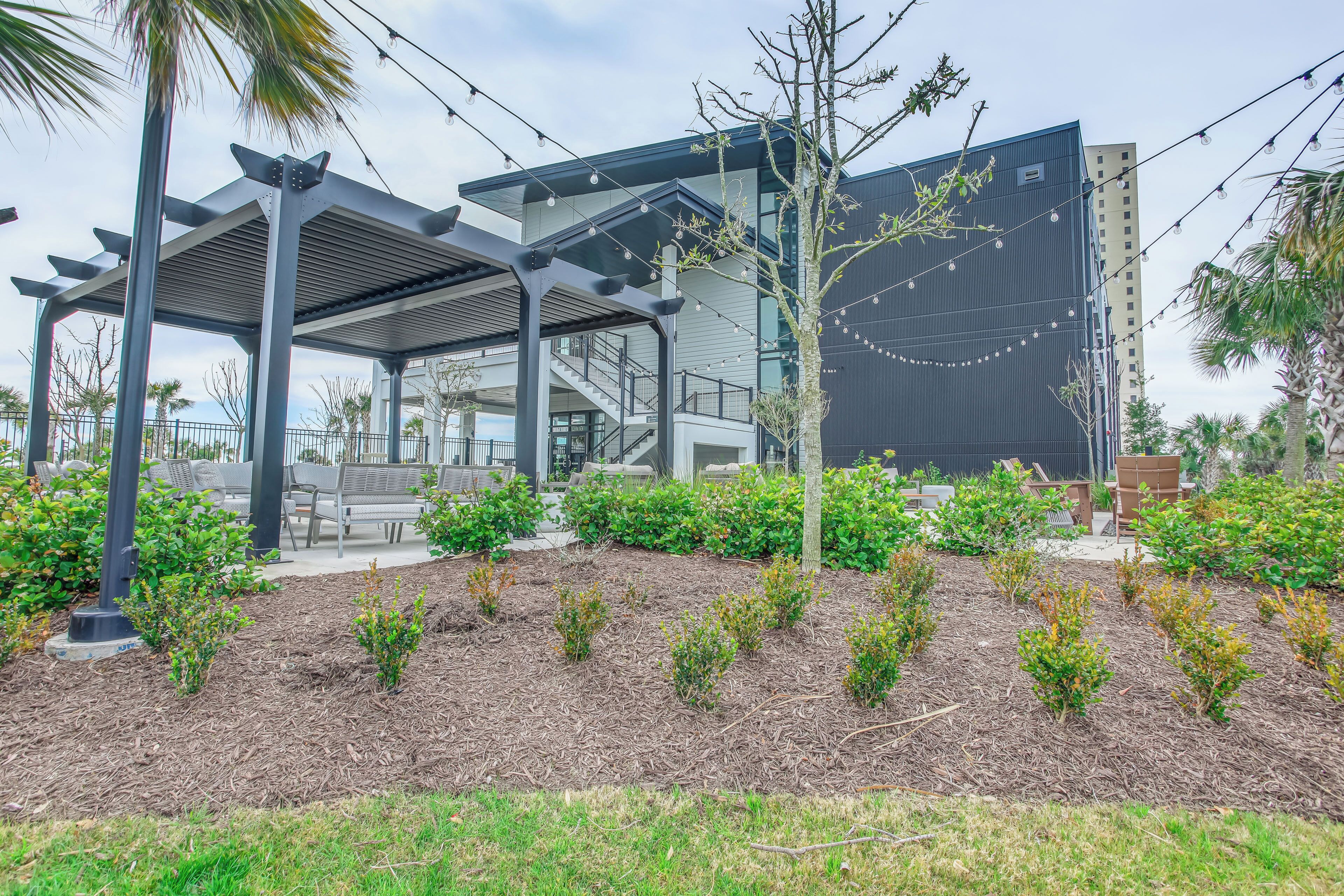A modern building with a covered outdoor area, a staircase, and a landscaped garden with small shrubs.
