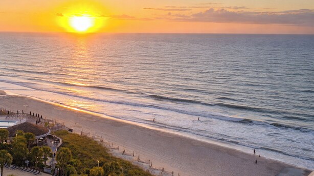 A beach with a sunset, ocean waves, and a building with a pool. - Warm Weather Escape w/ Pool Access in Myrtle Beach (Myrtle Beach)