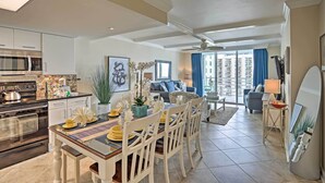 A modern kitchen with a dining area, a living room with a sofa and a view of the city, and a large window with curtains. - Warm Weather Escape w/ Pool Access in Myrtle Beach (Myrtle Beach)