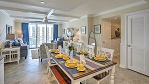 A dining area with a long table set for six, a sofa, and a view of a cityscape through large windows. - Warm Weather Escape w/ Pool Access in Myrtle Beach (Myrtle Beach)