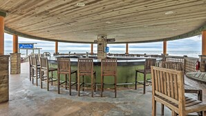 A covered outdoor seating area with wooden chairs and a bar, overlooking the beach. - Warm Weather Escape w/ Pool Access in Myrtle Beach (Myrtle Beach)