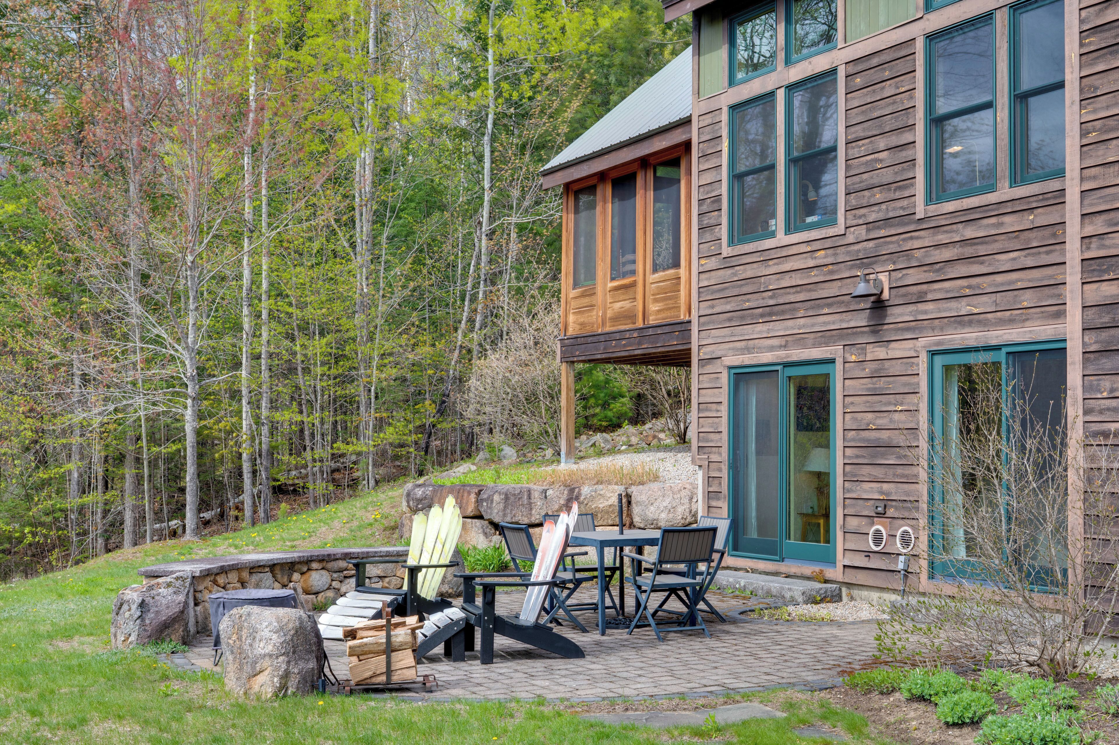 A wooden cabin with a stone fireplace, outdoor seating, and a view of the surrounding forest.