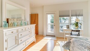 A well-lit room with a large mirror, a white dresser, a wooden door, a small table with a chair, and a window with blinds. - Seabrook Getaway w/ Balconies & Bay Views! (Seabrook)