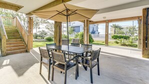 An outdoor patio with a wooden table and chairs, a large umbrella, and a staircase leading to an upper level. - Seabrook Getaway w/ Balconies & Bay Views! (Seabrook)