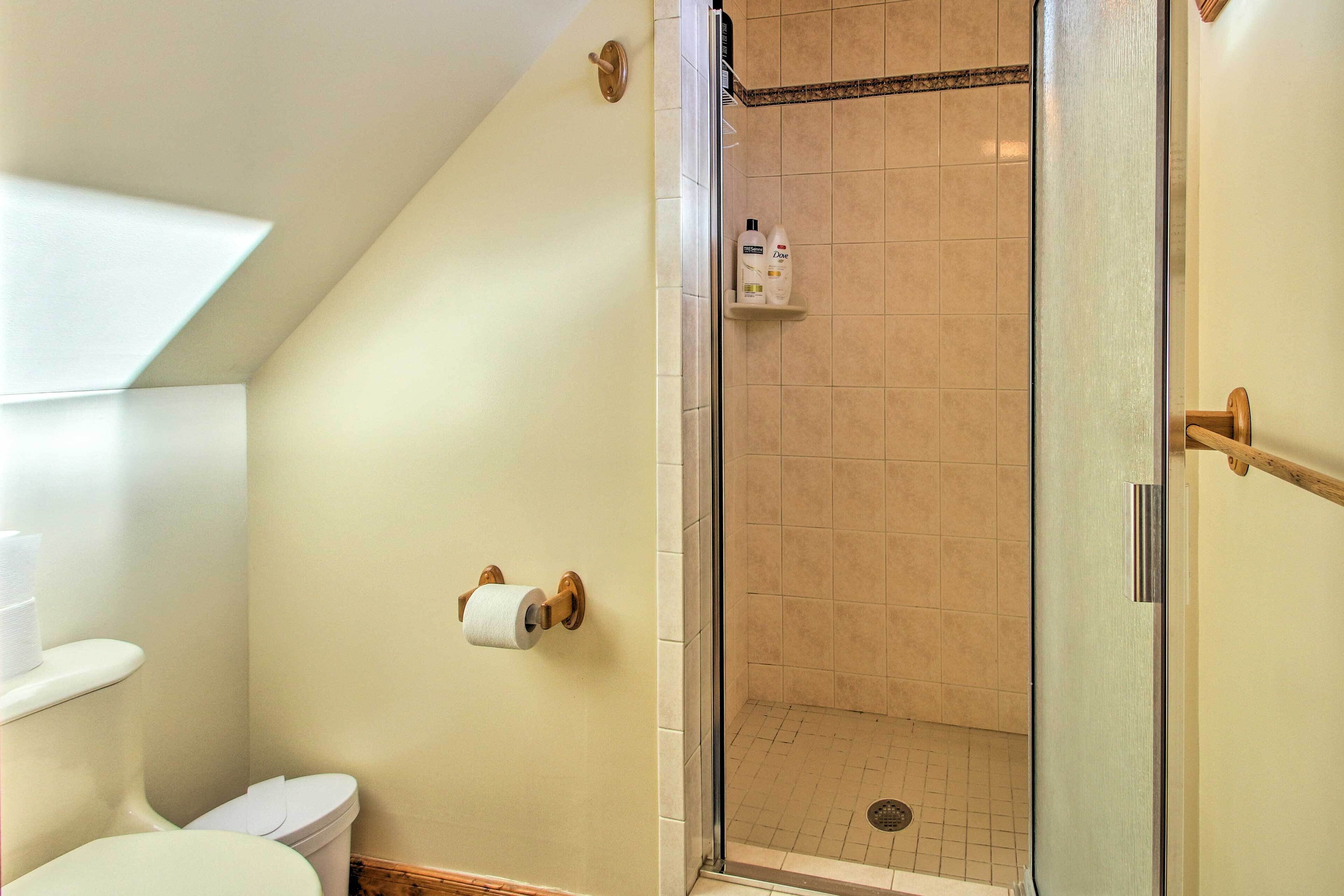 A bathroom with a toilet, a shower with a glass door, and toiletries on a shelf.