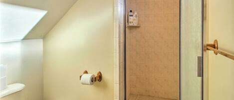 A bathroom with a toilet, a shower with a glass door, and toiletries on a shelf.