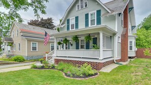 A two-story house with a porch, a brick foundation, and a small garden. - Family-friendly Glens Falls Home w/ Sun Porch (Glens Falls)