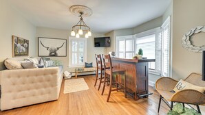 A cozy living room with a sofa, a dining area with wooden chairs, a kitchen counter, and a television mounted on the wall. - Family-friendly Glens Falls Home w/ Sun Porch (Glens Falls)