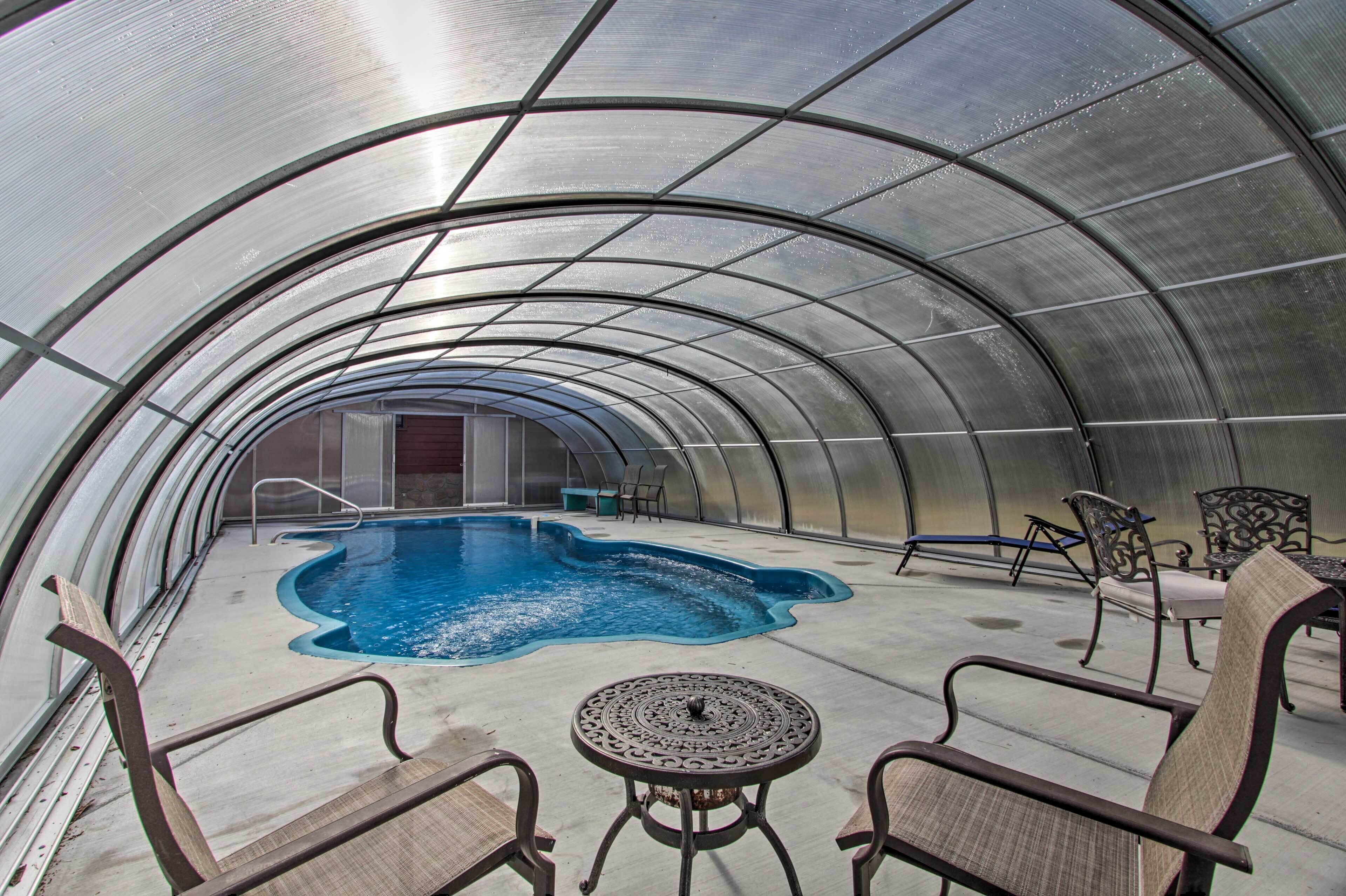 A covered swimming pool with chairs and a table, enclosed by a curved metal roof.