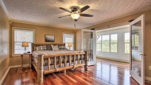 A bedroom with a wooden bed, a ceiling fan, and large windows. - Luxe Cabin w/ Covered Pool + Smoky Mountain Vistas (Sevierville)