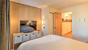 Ein Hotelzimmer mit einem Bett, einem Fernseher auf einer Holzkommode, einer Tür zu einem anderen Raum und einer Wandleuchte.