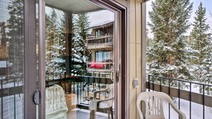 Ein Balkon mit Blick auf eine verschneite Landschaft, darunter ein Gebäude mit mehreren Balkonen und schneebedeckten Bäumen.