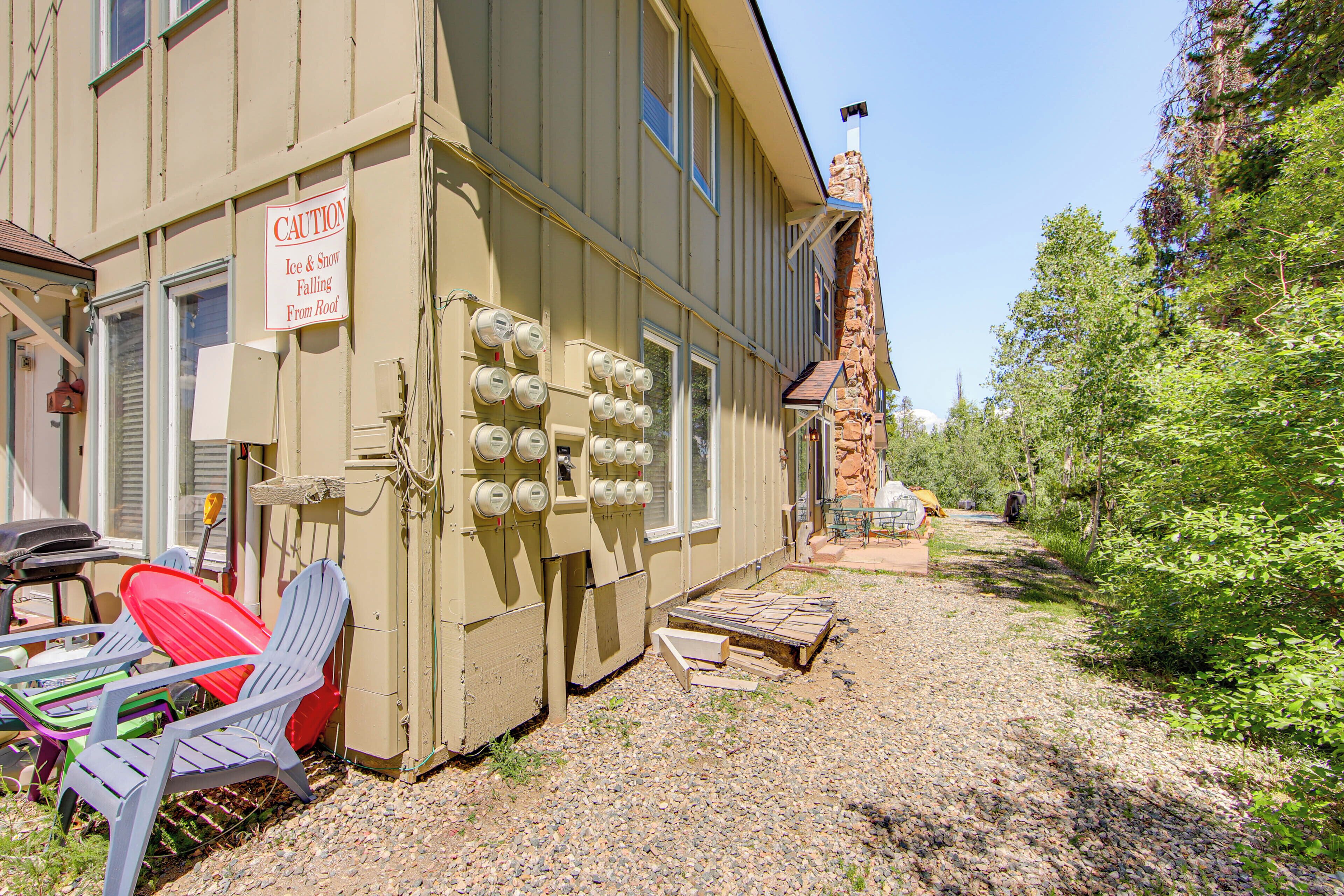 A building with a caution sign for ice and snow falling from the roof, outdoor seating with Adirondack chairs, and a gravel path.