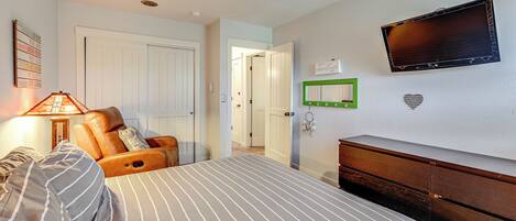 A bedroom with a bed, a chair, a dresser, a television, and a door leading to another room.