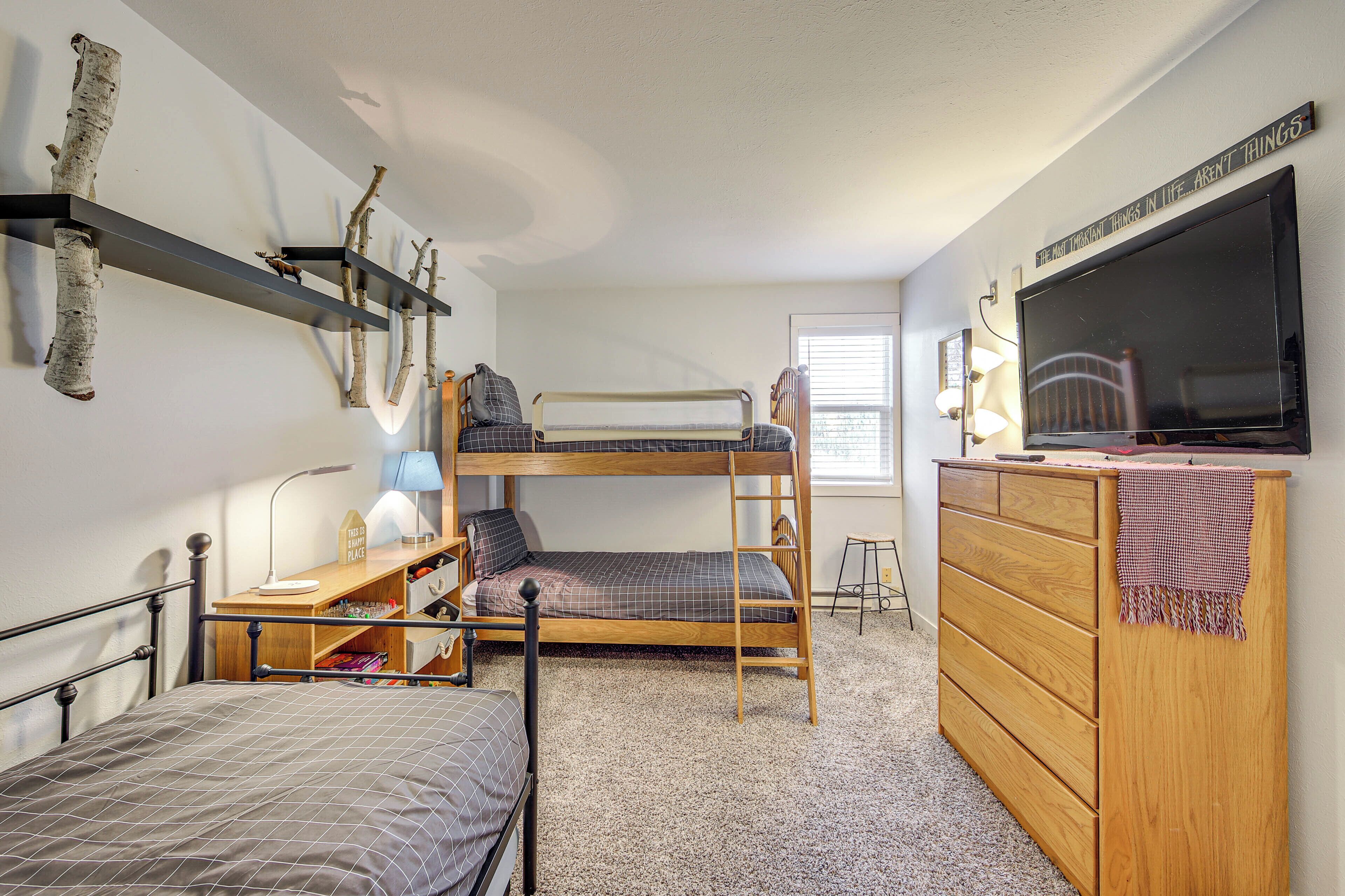 Ein gemütliches Schlafzimmer mit Etagenbetten, einer Holzkommode, einem Fernseher und einem Regal mit dekorativen Zweigen.