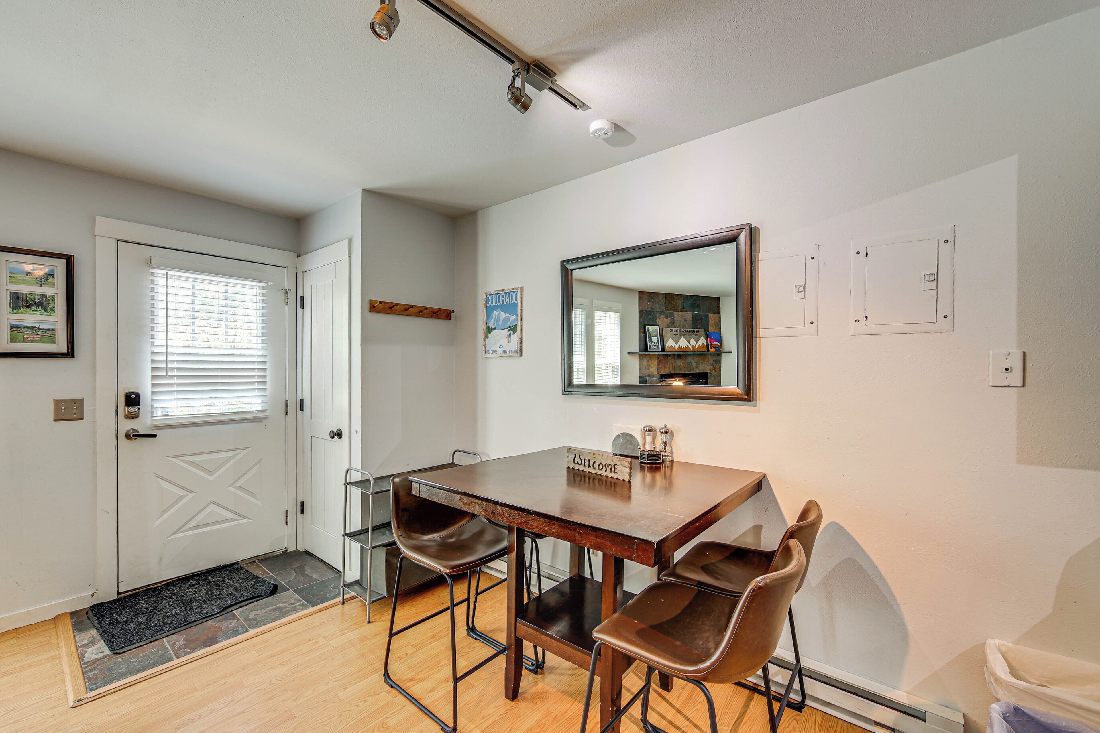 A dining area with a wooden table, four chairs, a welcome sign, a mirror, and a door with a window.