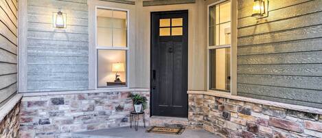 A house entrance with a black door, two windows with white frames, a stone wall, and a small table with a plant.