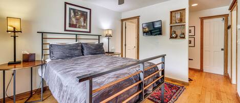 A bedroom with a bed, a ceiling fan, a TV, and a door.