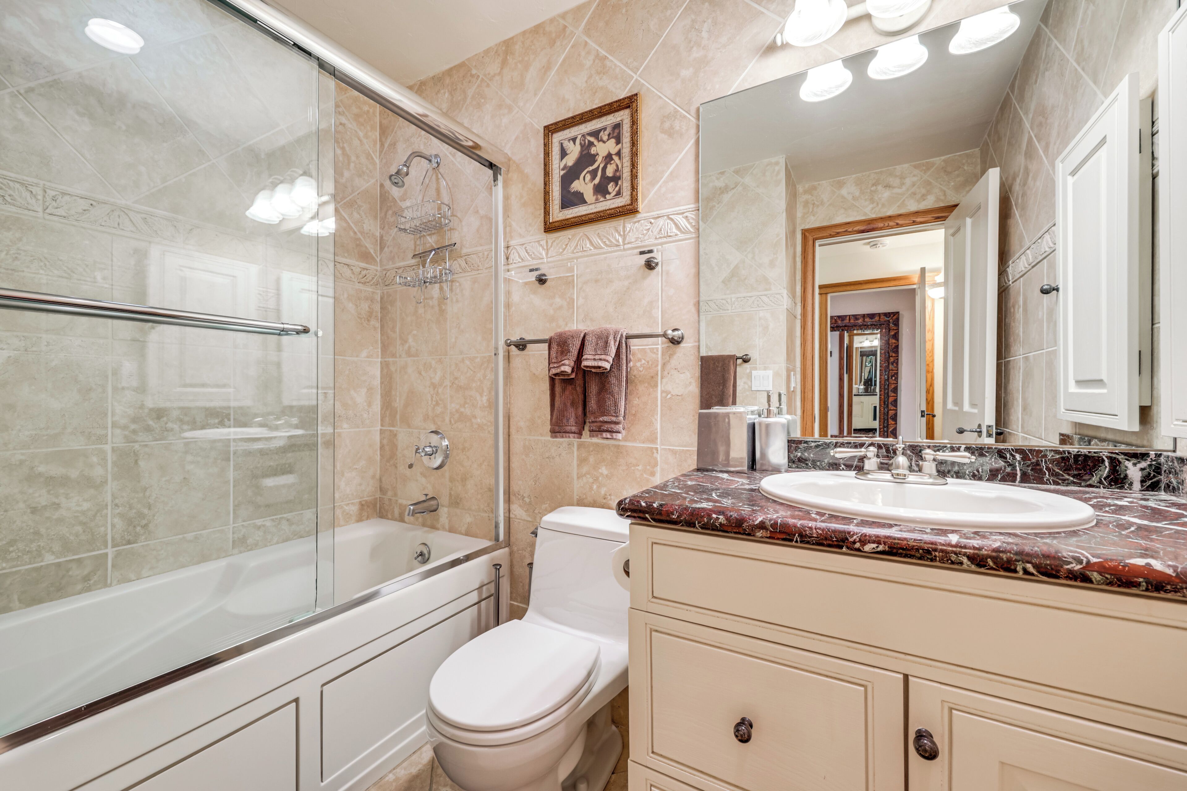 Une salle de bain avec une douche à parois de verre, des toilettes blanches, un lavabo en marbre et un grand miroir.