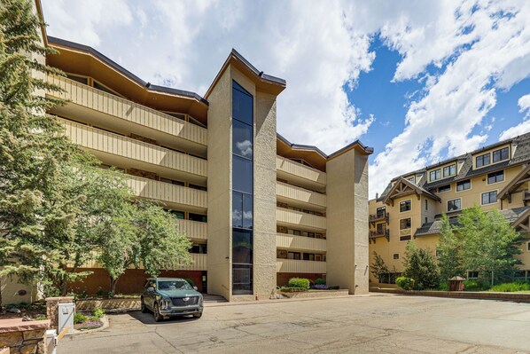 A multi-story hotel with a central tower, balconies, and a parking area.
