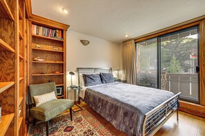 Un dormitorio con una cama grande, una estantería de madera, una silla y vistas por un amplio ventanal.