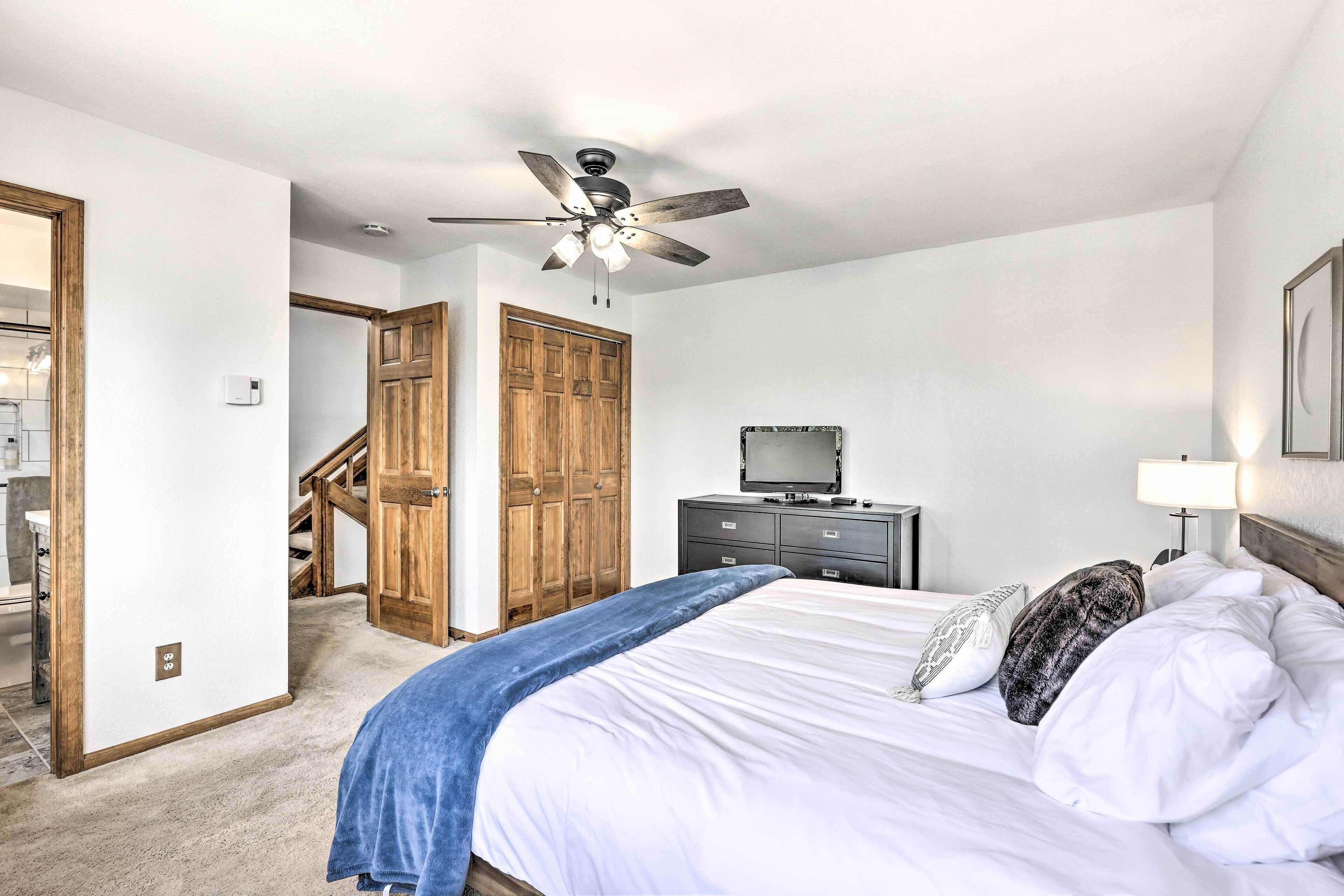 Un dormitorio con cama, ventilador de techo, televisor, cómoda y puerta de madera.