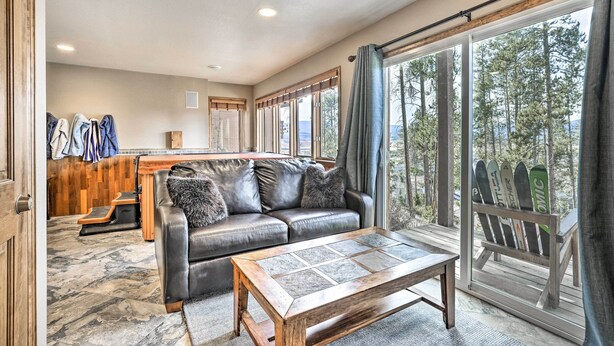 Un espacio de sala acogedor con un sofá de cuero, una mesa de centro y un soporte para esquíes junto a un ventanal con vistas a un bosque.