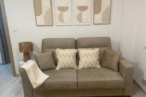 A beige sofa with two patterned pillows, a lamp, and abstract wall art. - 102B Poniente Mágico by R2R Consulting (Gijón)