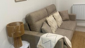 A neutral-toned living room with a sofa, a lamp, and a radiator. - 102B Poniente Mágico by R2R Consulting (Gijón)